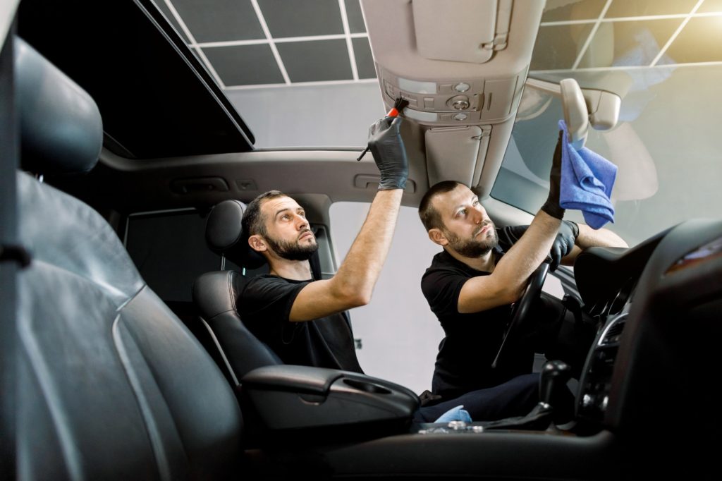 Professional auto detailing. Two men car service workers cleaning modern auto interior, plastic