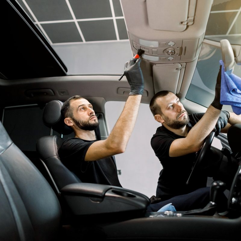 Professional auto detailing. Two men car service workers cleaning modern auto interior, plastic